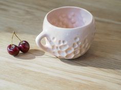 a small white cup with two cherries in it on a wooden surface next to a smaller one