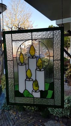 a stained glass window with three candles hanging from it's side, in front of a house