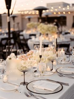 the table is set with white flowers and candles for an elegant wedding reception at night