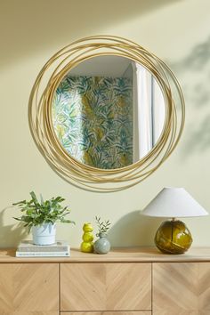 a mirror hanging on the wall above a dresser with vases and plants in front of it