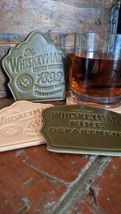 two coasters with whiskey labels on them sitting next to a glass filled with liquid