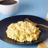 scrambled eggs on a black plate with a fork and cup of coffee next to it