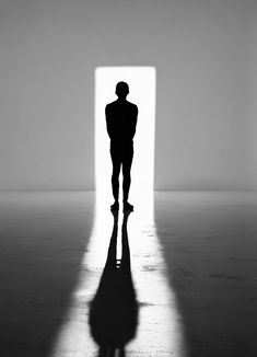 a man standing in front of a doorway with his shadow on the floor and back to the camera