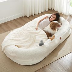 a woman laying in a dog bed on the floor with her brown and white dog