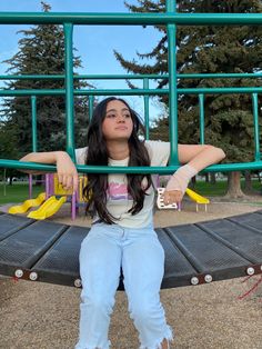 a woman sitting on top of a metal bench in front of a green playground structure