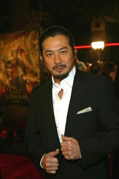 a man in a tuxedo standing on a red carpet with his hands clasped