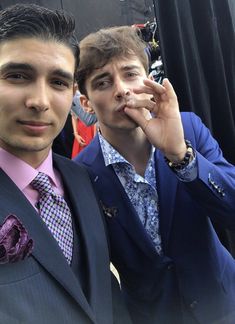 two men in suits and ties posing for the camera with one holding his hand up to his face