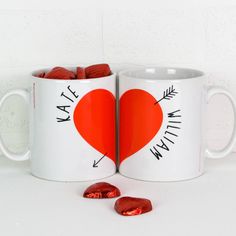 two coffee mugs with hearts and arrows on them, one is filled with candy