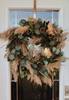 a wreath is hanging on the front door with pine cones and greenery around it