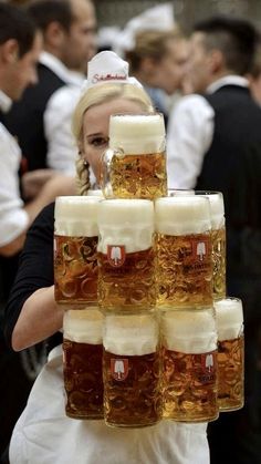 a woman is holding a large stack of beer mugs