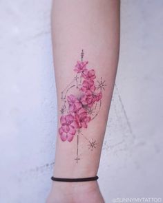 a woman's arm with pink flowers on it and stars around the wrist tattoo