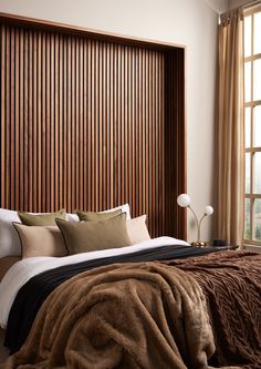 a large bed sitting next to a window covered in brown and white blankets on top of a wooden headboard