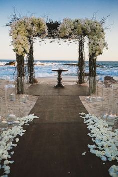 an outdoor ceremony set up on the beach with white flowers and candles in front of it