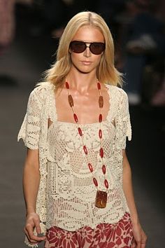 a woman walking down a runway wearing sunglasses and a white top with red flowers on it