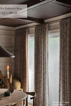 a dining room table with chairs and a lamp on it next to two windows covered in curtains