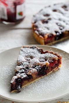 a slice of pie on a plate with powdered sugar and jelly in the background