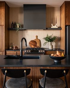 a kitchen with black counter tops and wooden cabinets, along with two stools in front of the sink