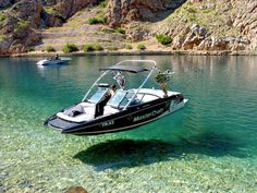 two motor boats in the water near some rocks and mountains, one is black and white