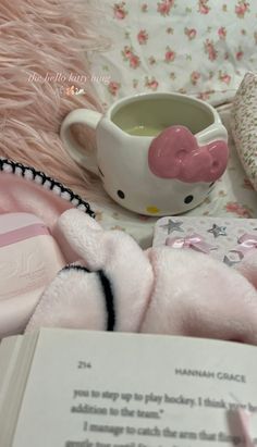 a pink teddy bear laying on top of a bed next to a cup and book