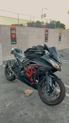 a black motorcycle parked in a parking lot next to a cement wall with graffiti on it