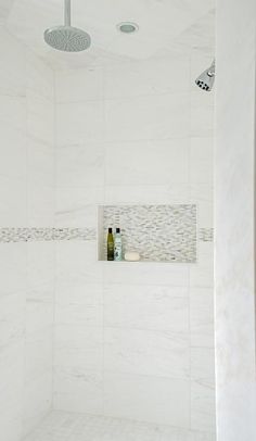 a white tiled bathroom with shower head and soap dispenser on the wall