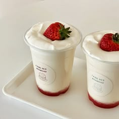 two yogurt cups with strawberries on top sit on a white serving tray