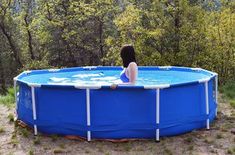 a woman sitting in the middle of a blue swimming pool surrounded by trees and grass