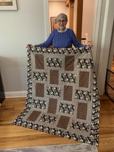 an older woman holding up a quilt on the floor