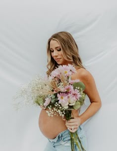 a pregnant woman holding a bouquet of flowers in front of her stomach while standing against a white backdrop