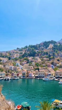 boats are parked on the water in front of some buildings and hills with trees around them