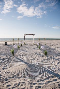 an outdoor ceremony setup on the beach with white linens and greenery in the sand