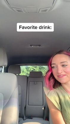 a woman with pink hair sitting in the back seat of a car and looking at the camera