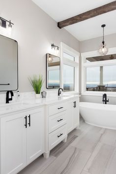 a white bathroom with two sinks and a bathtub in the middle, along with large windows