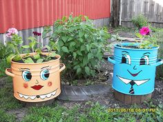 three pots with faces painted on them sitting in the grass next to flowers and plants