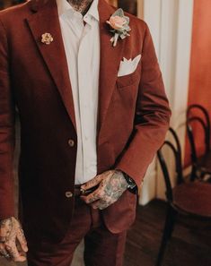 a tattooed man in a red suit and flower boutonniere