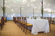 tables and chairs are set up in a tent for an outdoor wedding or reception with white tablecloths and yellow chair covers