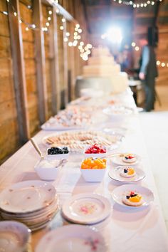 a long table with many plates and bowls on it, along with lights strung from the ceiling