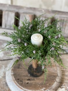 a small white candle sitting on top of a wooden stand with greenery in it