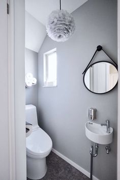 a white toilet sitting next to a bathroom sink under a round mirror on the wall