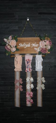 a wooden sign hanging from the side of a wall with ribbons and flowers on it