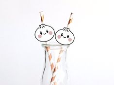 two straws with faces drawn on them sitting in a glass vase filled with liquid