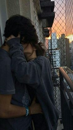 a man and woman hugging on the balcony of a building with cityscape in the background