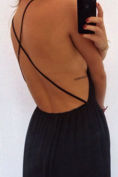 a woman with her back turned to the camera taking a selfie while wearing a black dress