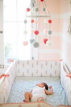 a baby laying in a crib with pom poms hanging from the ceiling