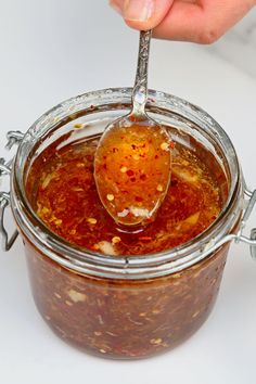 a person spooning some food out of a glass jar filled with sauce and seasonings