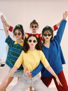 three young women wearing sunglasses and standing in front of a wall with their arms up