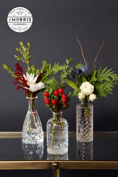 three glass vases with flowers and greenery in them on top of a table