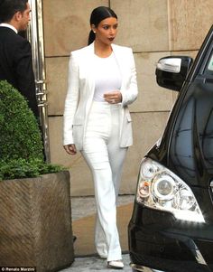 a woman in white is walking past a car