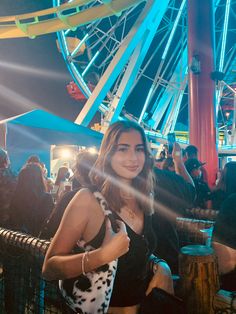 a woman standing in front of a ferris wheel at an amusement park with her hand on her hip