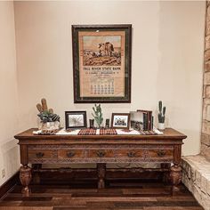 a wooden desk with pictures on it in front of a stone wall and framed artwork